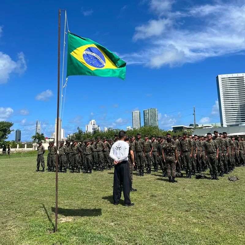 Tropa do Exército em formação diante da bandeira do Brasil, com um instrutor da Federação de camiseta branca à frente